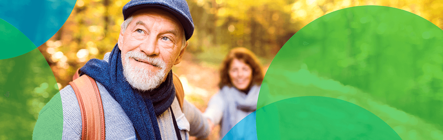 Older man in a scarf, hat and sweater holding the hand of a woman in a forest. Blue and green circles border them