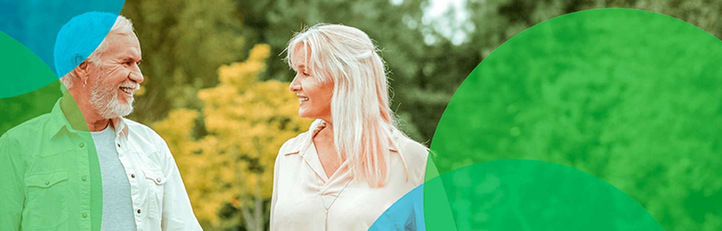 Image of an older man and woman smiling at each other while outdoors. Blue and green circles border them